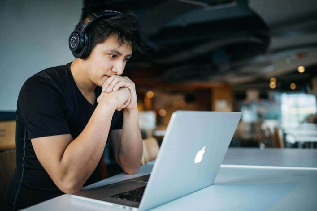 young man wearing black shirt, headphones, white mac laptop